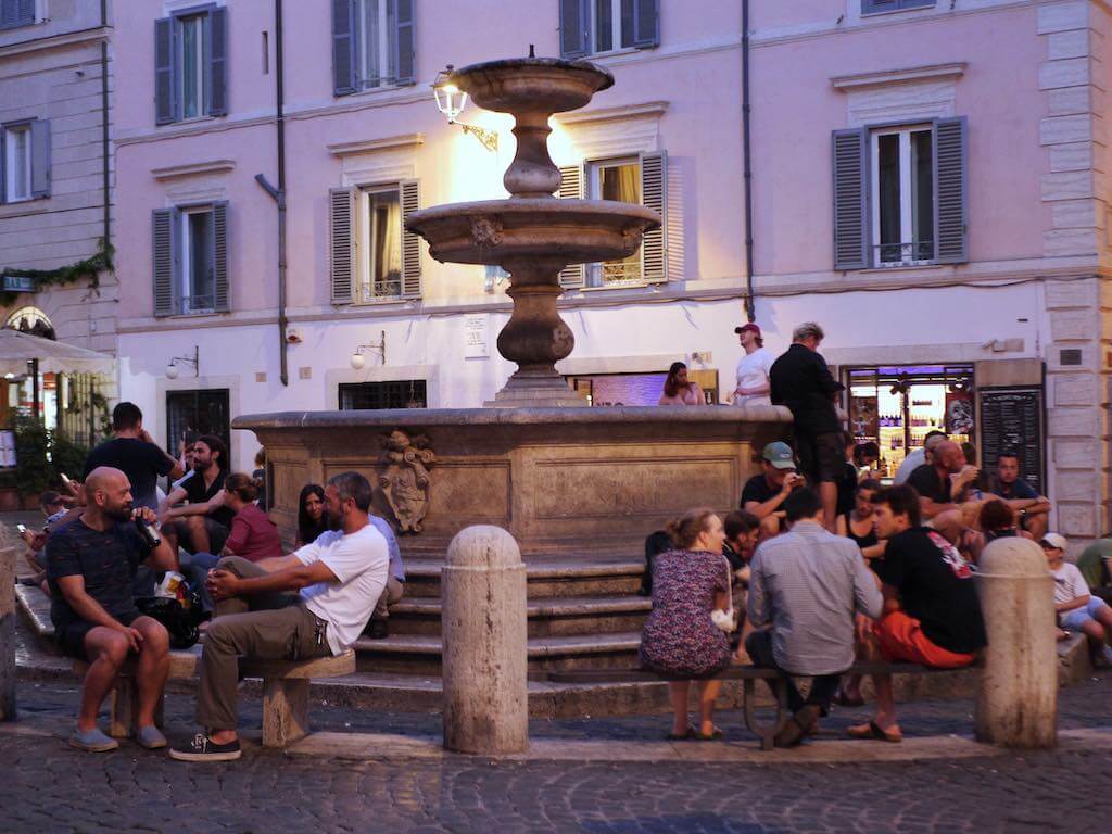 Piazza della Madonna di Monti in the Monti neighborhood in Rome near Colosseum is a gathering hub for locals and travelers that sit and chat near its central fountain during the evening.