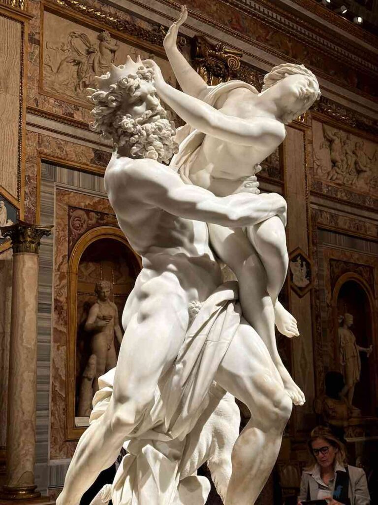 A dramatic marble sculpture of a muscular man lifting a struggling woman in his arms, her body twisting as she tries to escape, while his hands press into her skin, emphasizing movement and tension.